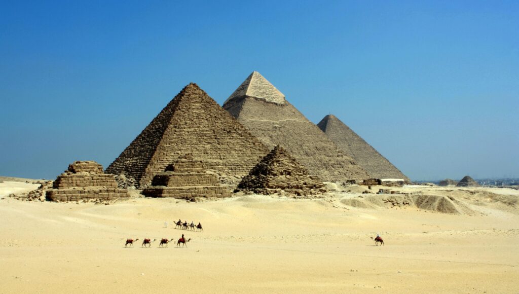 pexels-photo-71241-71241 Capture of the iconic Pyramids of Giza under a clear blue sky with camels traversing the sandy desert.